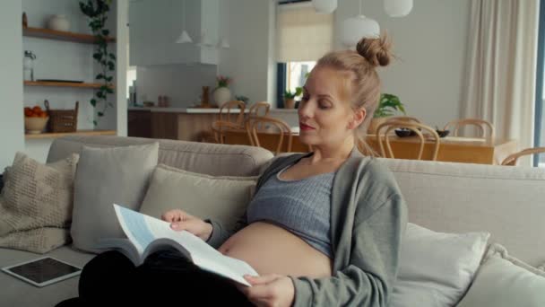 Λευκή Έγκυος Γυναίκα Κάθεται Στον Καναπέ Και Διαβάζει Ένα Βιβλίο — Αρχείο Βίντεο
