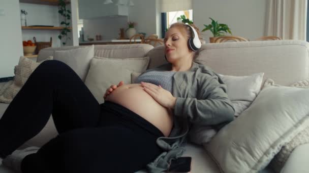 Λευκή Έγκυος Γυναίκα Ξαπλωμένη Στον Καναπέ Και Ακούγοντας Μουσική — Αρχείο Βίντεο