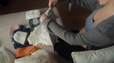 Hamile bir kadının bebek kıyafetlerini katlarken yüksek açılı görüntüsü.