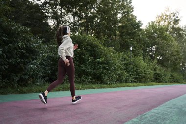 Parkta koşan kadının geniş açılı görüntüsü.