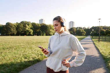Park 'ta cep telefonunu karıştıran ve kulaklık takan bir kadın.
