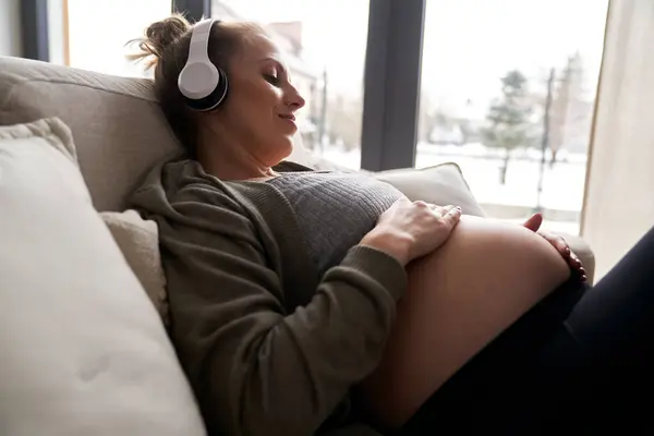白人孕妇躺在沙发上听音乐 — 图库照片