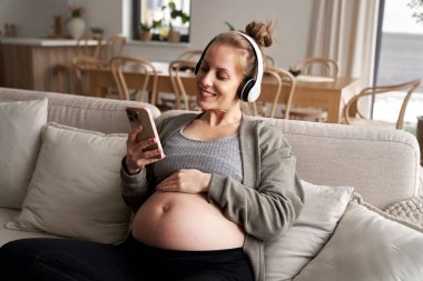Kafkasyalı hamile kadın kanepede oturup müzik dinliyor.