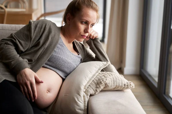 焦虑的孕妇躺在沙发上摸着肚子 — 图库照片