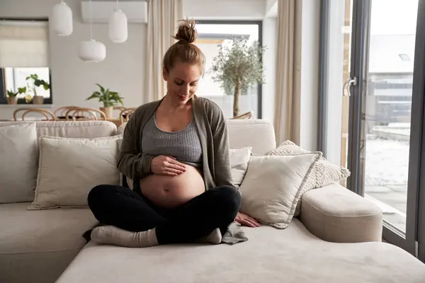 白种人孕妇坐在沙发上摸着肚子 — 图库照片