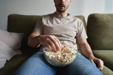 Patlamış mısır yiyip televizyon izleyen bir adam.