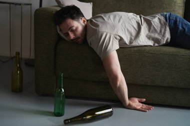 Sarhoş adam boş şişelerin arasında kanepede yatıyor.