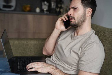 Adam dizüstü bilgisayar kullanıyor ve koltukta otururken arıyor.