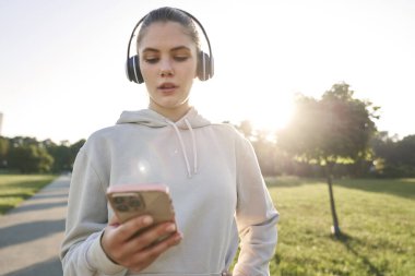 Spor kıyafetli bir kadın elinde cep telefonuyla pistte