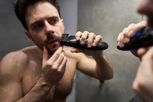 Caucasian man using electric shaver in the domestic bathroom