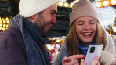 Genç çift geceleri Noel pazarında telefonlarını karıştırıyor.
