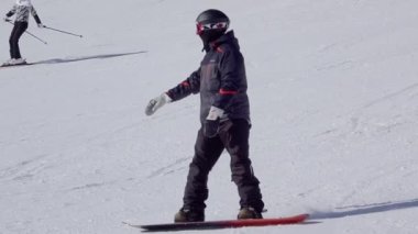Slovakya. Jasna kayak merkezinde güneşli bir kış günü. Genç bir çift - bir snowboardcu ve bir kız kayakçı geniş bir kayak yamacından aşağı iniyorlar. Yavaş çekim