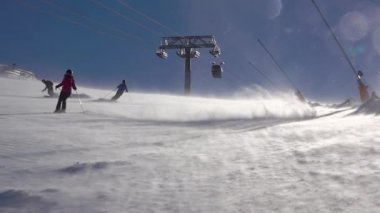 Güneşli bir kayak yamacında kar fırtınası. Kayak merkezi Jasna, Slovakya 'da. Birkaç kayakçı yavaş hareket ediyor. Yavaş çekim