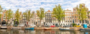 Hollanda 'da. Amsterdam 'da güneşli bir yaz günü. Kanal rıhtımının manzarası. Tekneler ve arabalar tipik Hollanda binalarının önüne park edilmiştir.