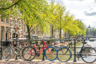 Hollanda, Amsterdam - 24 Eylül 2021: güneşli yaz günü. Kanalın üzerindeki köprüye bisikletleri park ettim. Rıhtımda küçük bir kafe.