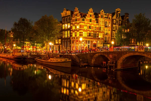 在阿姆斯特丹运河的夏夜用灯光跳舞的荷兰人的房子 有室外餐桌的酒吧 系泊的旧船 — 图库照片