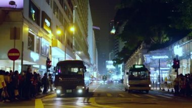 Hong Kong. Şehir kavşağında gece trafiği. Arabalar, otobüsler ve yayalar.