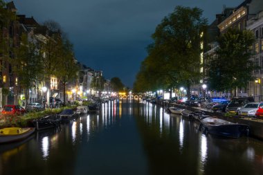 Hollanda 'da. Amsterdam 'ın rıhtımında bir yaz gecesi. Fenerler ve park halindeki arabalar. Kanalın kıyısına demirlemiş tekneler