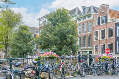 Hollanda 'da. Amsterdam 'da yaz günü. Kanal boyunca çiçek köprüsünün kenarına birkaç bisiklet park edilmiş.