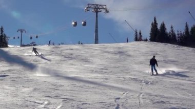 Kış Slovakya. Jasna kayak merkezindeki Tatras 'ta güneşli bir gün. Birkaç kayakçı arka planda bir kayak asansörüyle yamaçtan iniyor. Parlak güneşli hava. Yavaş çekim