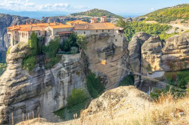 Yunanistan. Kalambaka 'da güneşli bir yaz günü. Uçurumunda kırmızı çatıları ve teleferiği olan bir manastır.