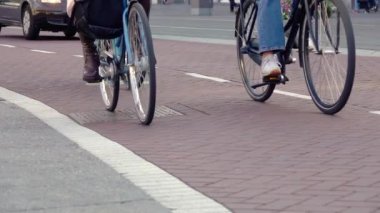 Hollanda 'da. Amsterdam caddesinde kaldırım döşemesi. Bisiklet yolunda birkaç bisikletçi var. Tekerlekler ve pedallar yakın çekim. Yavaş çekim