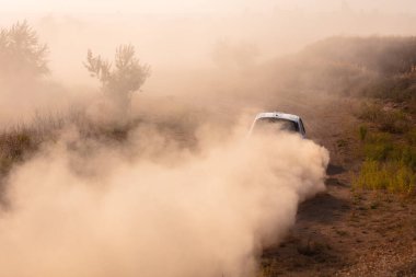 Güneşli bir yaz akşamı. Toprak yarış pisti. Ralli arabası toz bulutu yaratır
