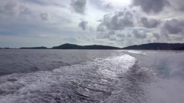 Akşamları okyanus ve ufuktaki tepe kıyısı. Dramatik gökyüzünde bulutlar. Güçlü bir dış motorun uyanışı. Yavaş çekim