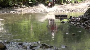 Orman yolunda güneşli bir yaz günü. Motosikletli bir Enduro sürücüsü bir sürü sıçramayla küçük bir nehri geçer. Yavaş çekim