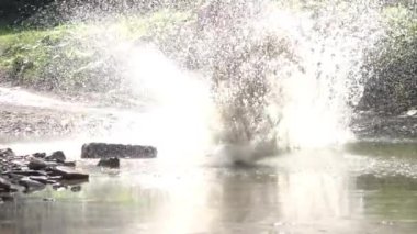 Yazın yaprak döken ormanda güneşli bir gün. Enduro binicisi toprak yolda motosiklet sürüyor ve bir sürü sıçramayla küçük bir nehri geçiyor. Yavaş çekim