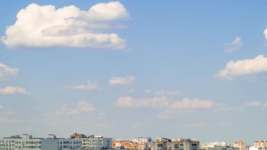 Güneşli bir günde mavi gökyüzü şehrin çatılarında. Bulutlar hızlı hareket ediyor, binaların üzerine gölge düşürüyor. Zaman aşımı