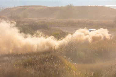 Güneşli bir yaz günü. Büyük bir toz bulutu toprak yolda bir rali arabasını gizliyor.