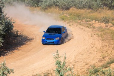 Güneşli bir yaz günü. Toprak yolda geniş bir dönüş. Mavi rali arabası toz bulutları oluşturur