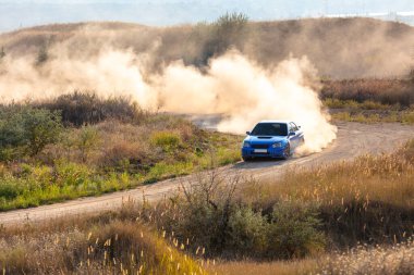 Güneşli bir yaz günü. Mavi rali arabası toz bulutları oluşturur. Toprak yolda dar bir virajı tamamlar.