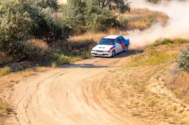 Güneşli bir yaz günü. Beyaz rali arabası toprak yolda keskin bir dönüş yapmak üzere.