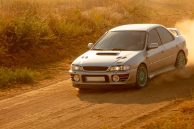 Güneşli bir yaz akşamı. Toprak yolda spor araba bir toz bulutu yükseltir