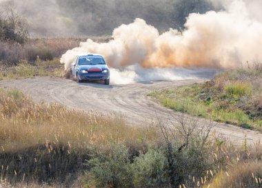 Güneşli bir yaz günü. Toprak yolda keskin bir dönüş yapan bir ralli arabası toz bulutunu kaldırır.