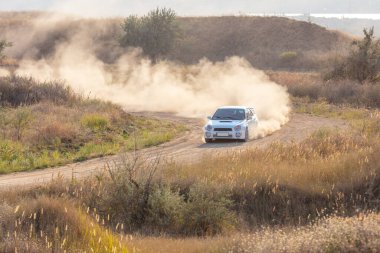 Bozkırlarda güneşli bir yaz günü. Toprak bir yolda keskin bir virajda beyaz spor araba ve toz bulutu