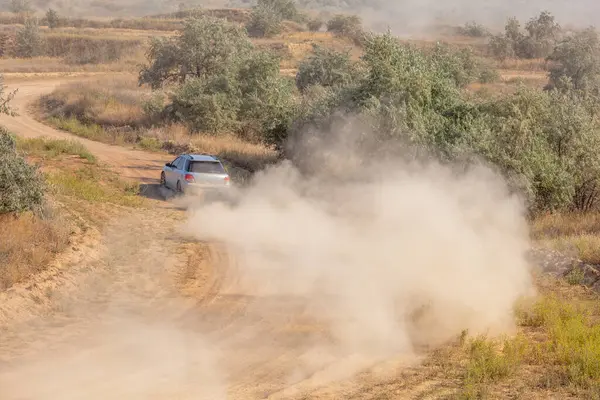 Bozkırlarda güneşli bir yaz günü. Bir rali arabası toprak yolda giderken bir toz bulutu kaldırır.