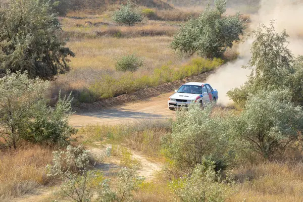 Bozkırlarda güneşli bir yaz günü. Toprak yolda tozlu bir rali arabası sürüyor