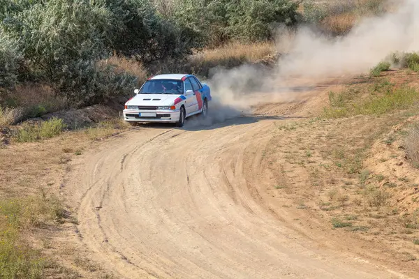 Bozkırlarda güneşli bir yaz günü. Bir rali arabası bir dönemece giriyor toprak bir yolda yuvarlanıp tozlanıyor.