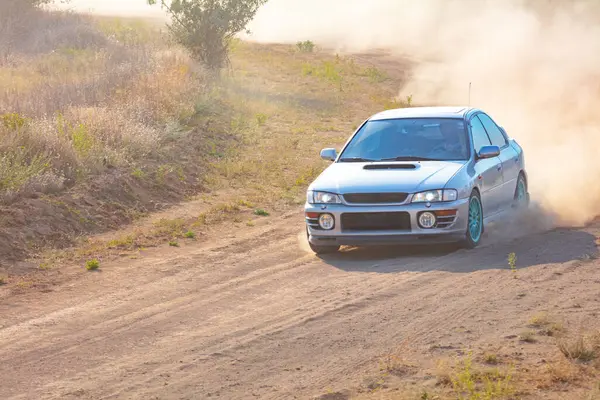Bozkırlarda güneşli bir yaz günü. Bir rali arabası toprak bir yolda toz bulutu kaldırır.