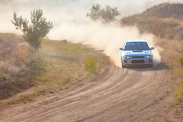 Bozkırlarda güneşli bir yaz günü. Bir rali arabası toprak bir yolda dönerken toz bulutu yapar.