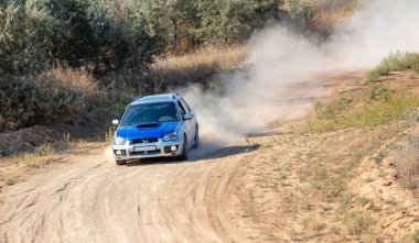 Bozkırlarda güneşli bir yaz günü. Çamurlu toprak yolda keskin bir viraj etrafında bir rali arabası sallanıyor.