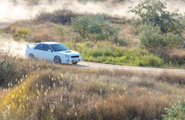 Bozkırlarda güneşli bir yaz günü. Arka kanadı olan beyaz bir rali arabası kuru toprak bir yoldan çıkarken toz bulutu yaratır.