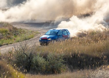 Bozkırlarda güneşli bir yaz günü. Bir rali arabası kuru toprak yolda toz bulutu yaratır.