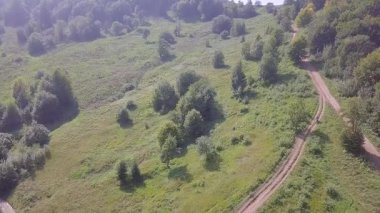 Yeşil ağaçlık tepelerde güneşli bir yaz günü. Kirli bir patika boyunca bir motosiklet sürücüsü. Hava görünümü