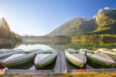 Avusturya 'da yaz gündoğumu. Dağ gölünün ayna gibi yüzeyi ve eğlence tekneleri için park yeri.