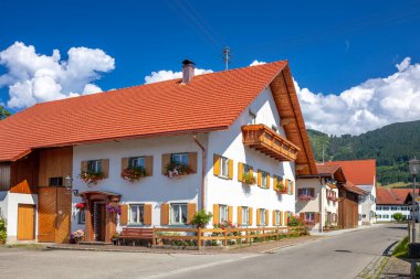 Avusturya yazı. Küçük bir kasabada güneşli bir gün. Mavi gökyüzünde tipik evleri ve resimli bulutları olan bir sokak.