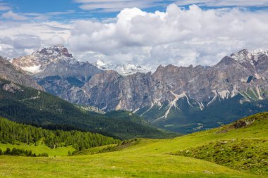 Karla kaplı sıradağlar, dramatik yaz bulutları altında yeşil ormanlar ve çayırlar üzerinde yükseliyor.